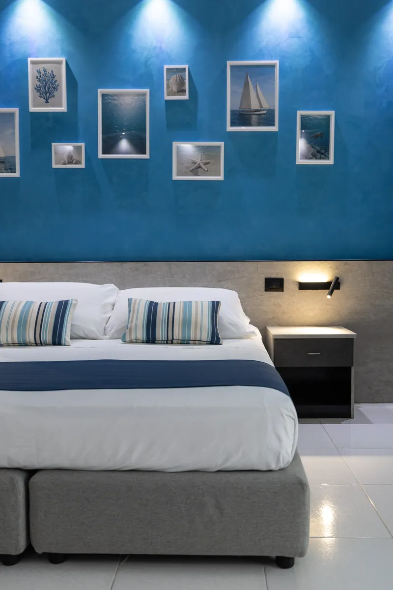 Letto matrimoniale sotto una parete blu con quadri del mare