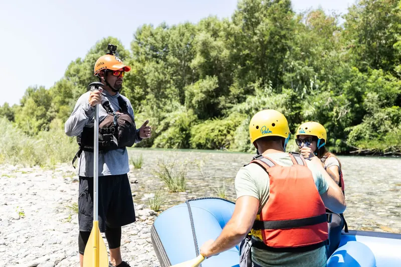 Guida di rafting che dà istruzioni a due ospiti con casco e giubbotto sul fiume